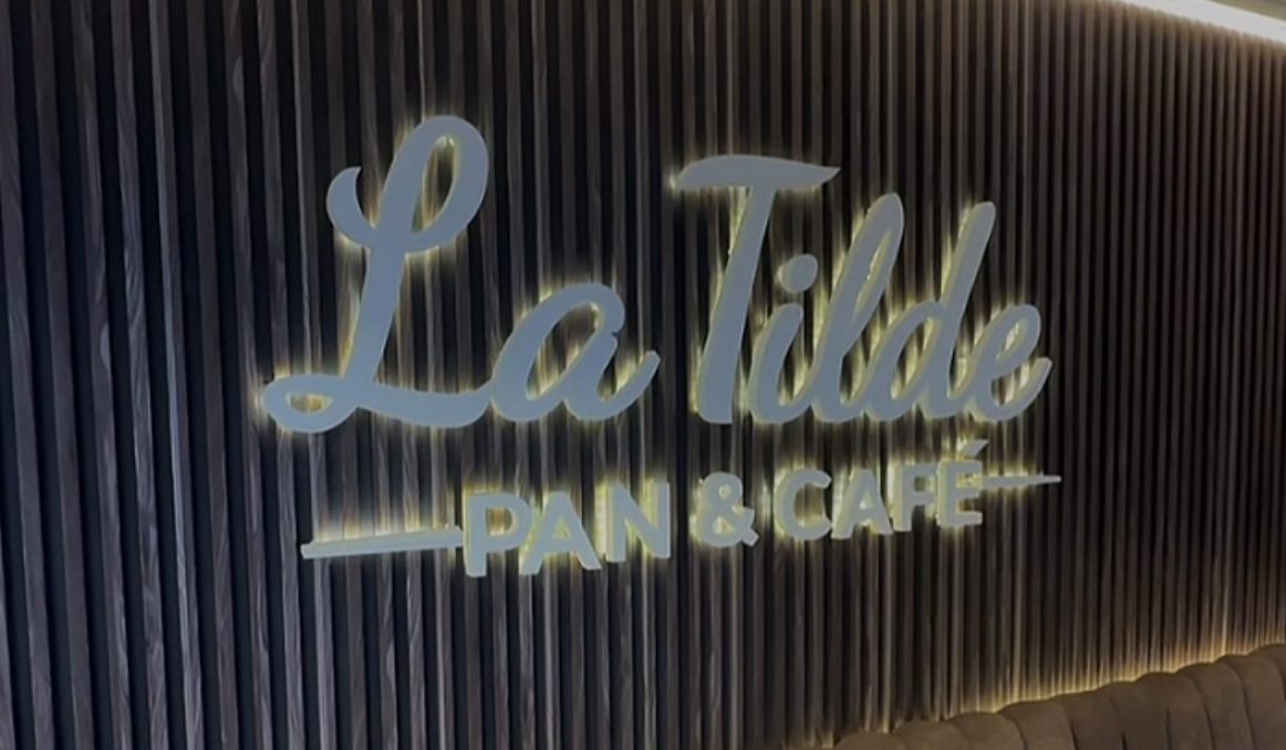Cartel iluminado de La Tilde, Pan & Café, sobre la pared de listones de madera del salón.